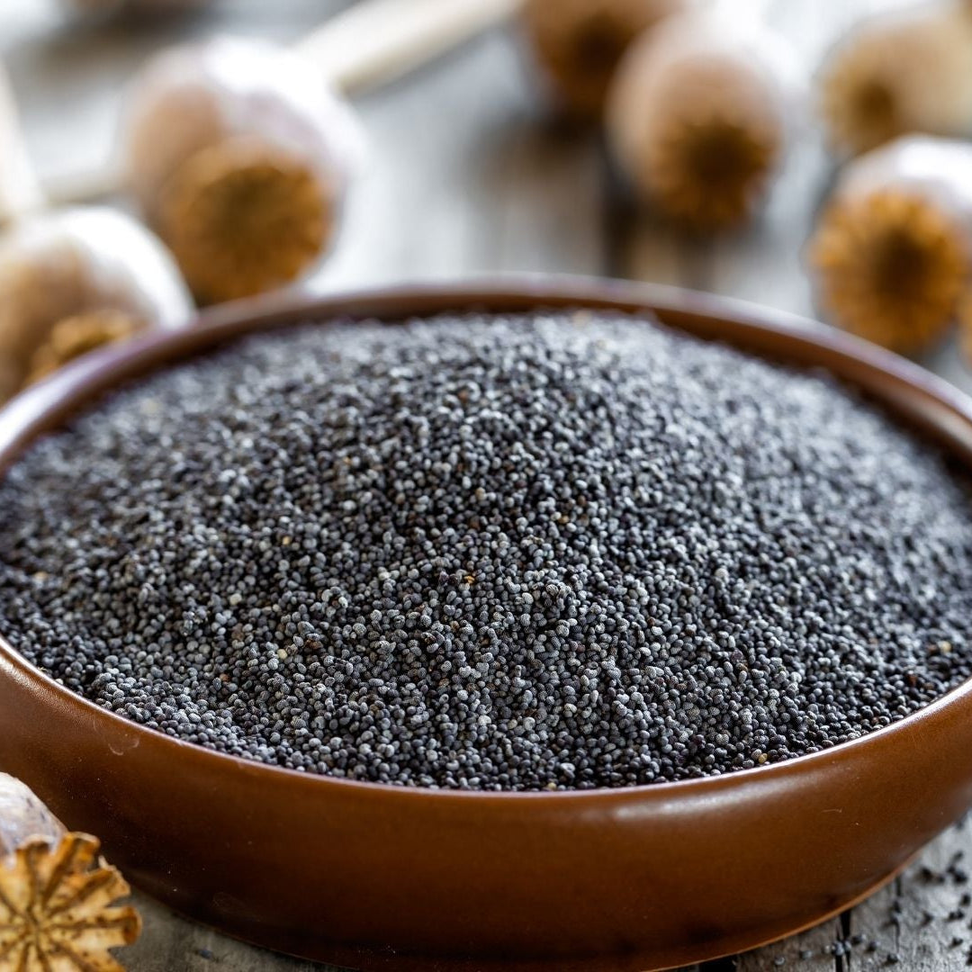 Bowl of poppy seeds with poppy flowers on a wooden surface