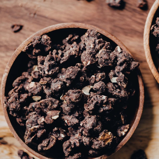 Two wooden bowls filled with dark brown dried herbs on a wooden surface.